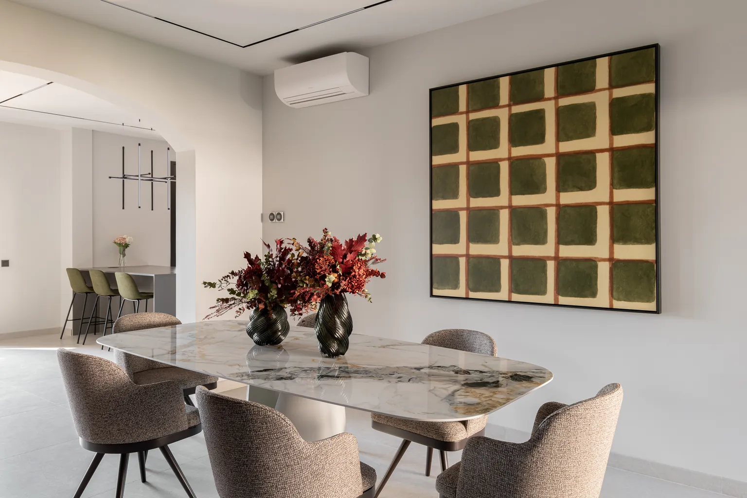 Dining room with a marble-effect porcelain table, upholstered chairs, a large painting and an arch opening onto the kitchen