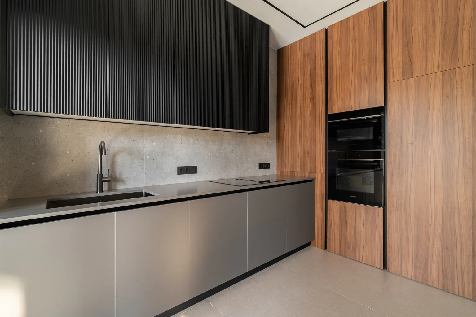 Bespoke kitchen with black fluted upper cabinets, grey base units, wood-look tall units with built-in ovens and a stone-effect splashback