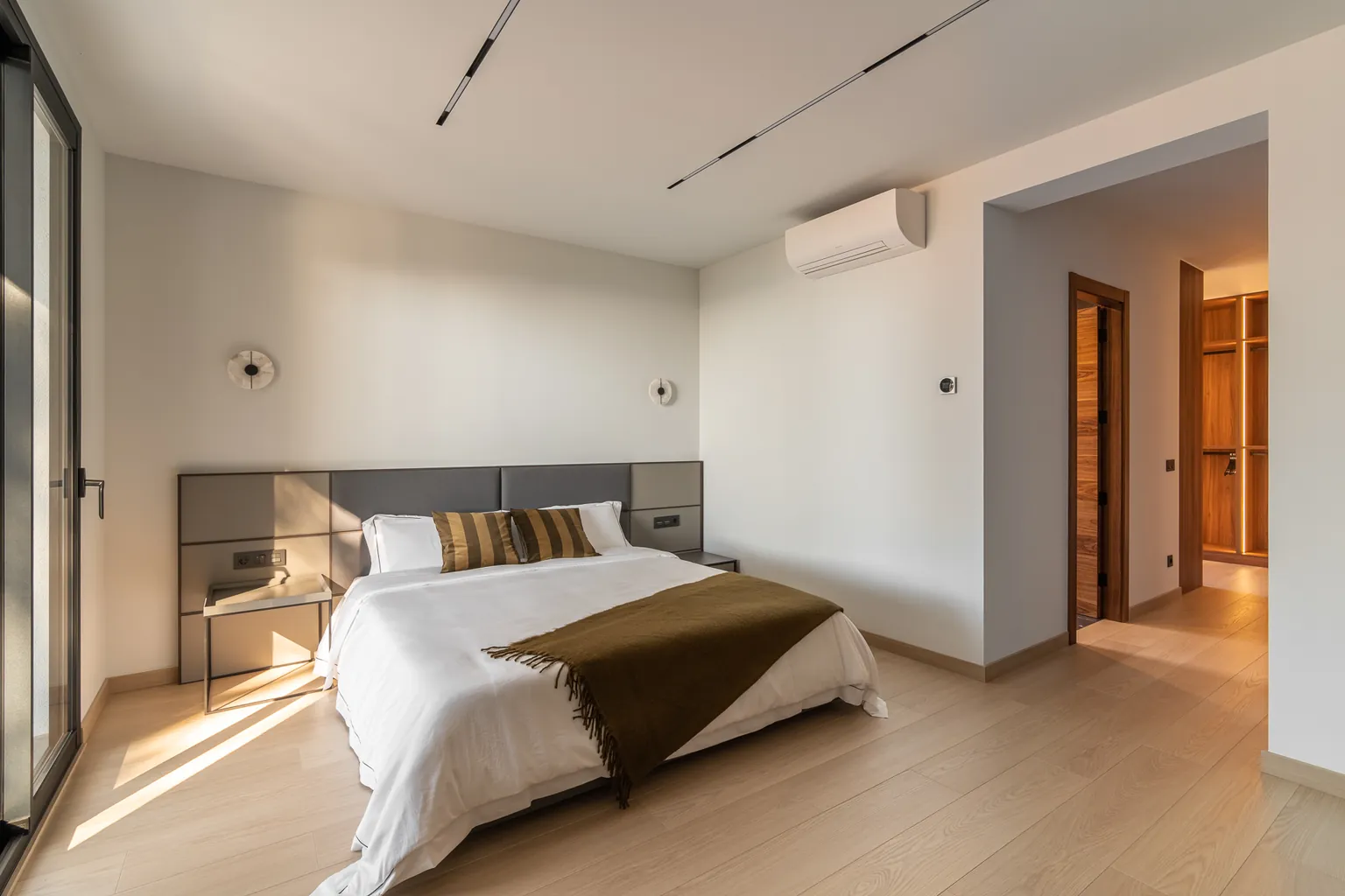Bedroom with a panelled upholstered headboard, parquet, magnetic tracks on the ceiling and a view of the dressing room