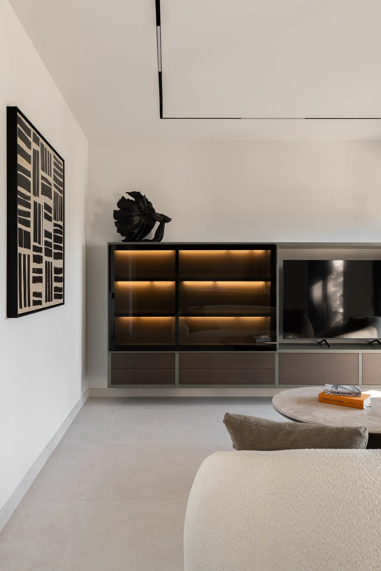 Bespoke living room unit with lit glass cabinets, a television, a black sculpture and a bouclé sofa