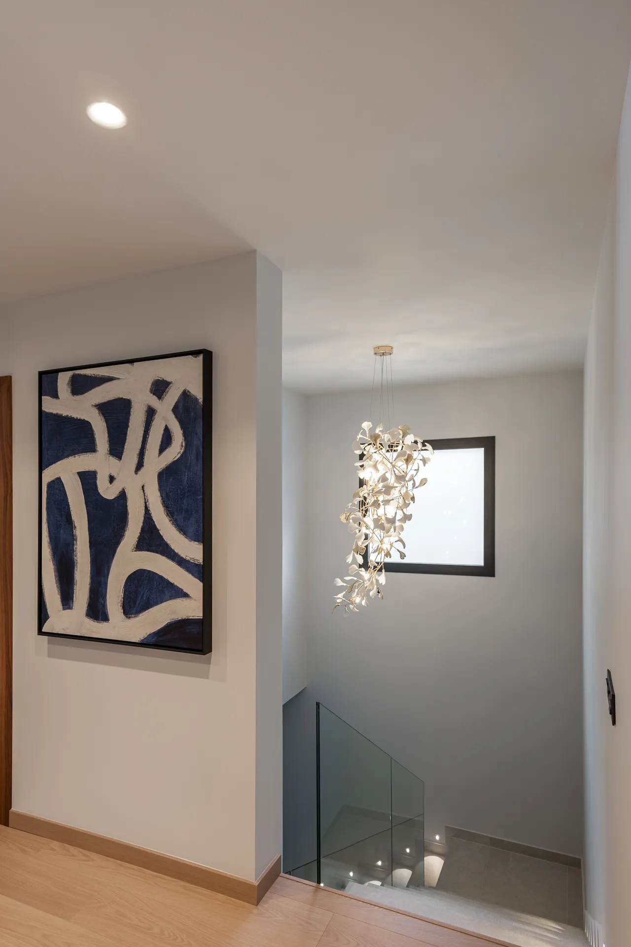 Staircase with a glass balustrade, a pendant lamp of white leaves and an abstract painting in blue