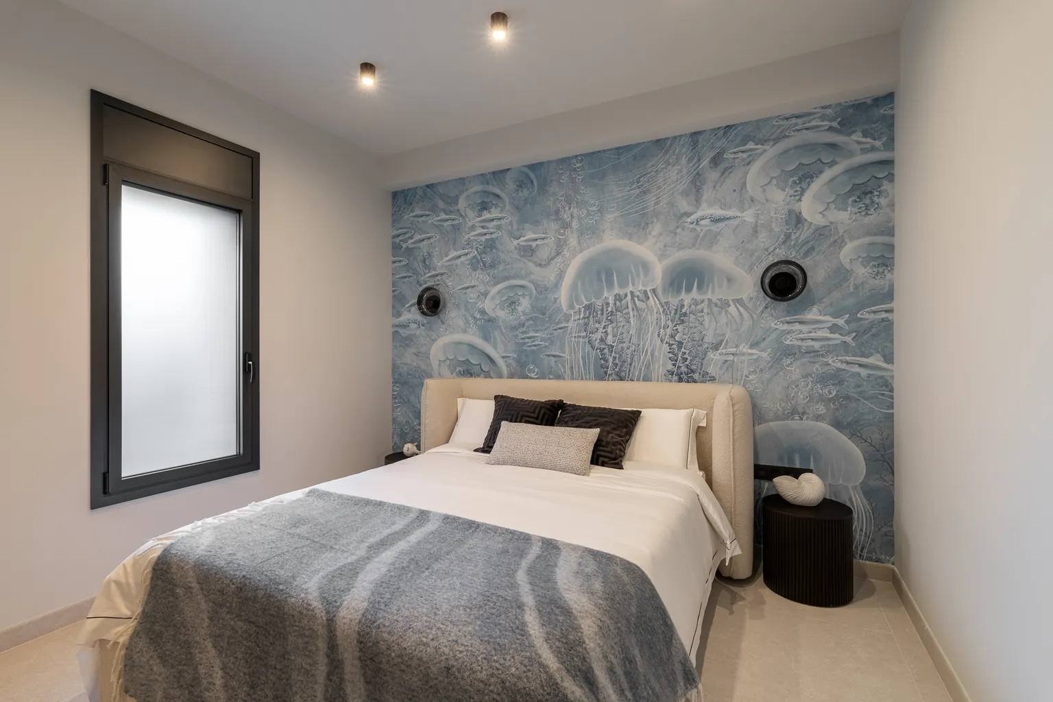 Bedroom with a jellyfish mural in shades of blue on the headboard wall, an upholstered bed and a black bedside table