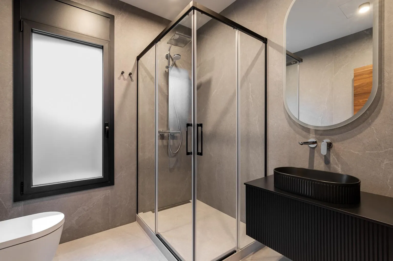 Bathroom with stone-effect porcelain, a corner shower with a black-framed screen, a black fluted wall-hung vanity and an oval backlit mirror