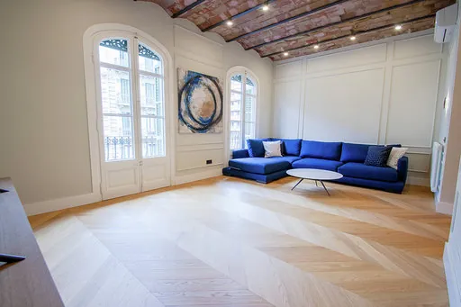 Living room of a renovated apartment in Barcelona's Eixample with a Catalan brick-vault ceiling, herringbone oak parquet, two balconies and a blue sofa