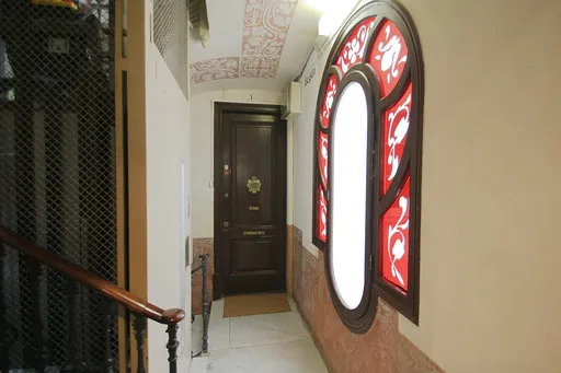 Staircase landing of the building with a red oval stained-glass window, a painted ceiling and a dark wooden door