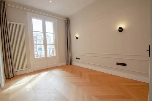 Room with wall mouldings, wall lights, a column radiator, curtains and a balcony, with herringbone parquet