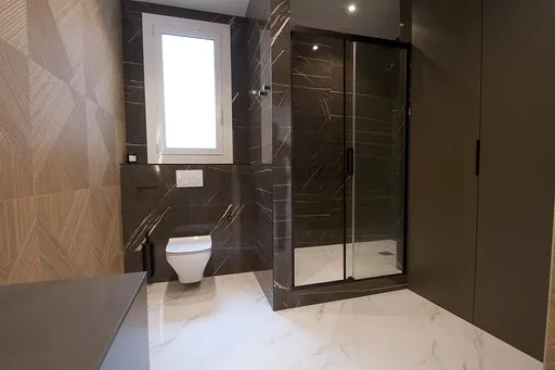 Bathroom with a black marble-effect porcelain shower, a black-framed screen, a wall-hung toilet, a window and a grey wardrobe
