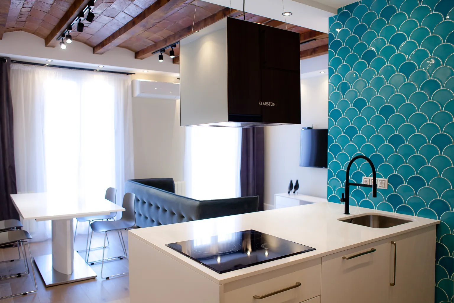 Living room with open kitchen in a renovated apartment in central Castelldefels: white island, turquoise fish-scale tiles, brick vaults and wooden beams