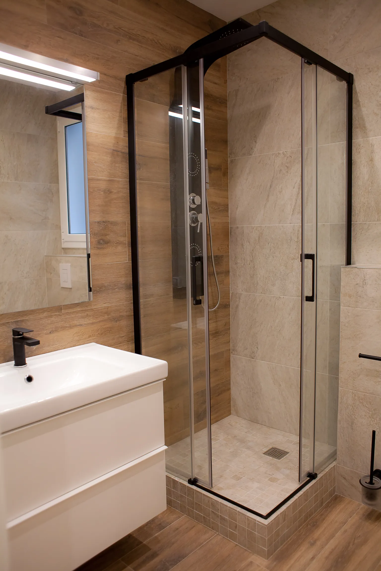 Baño con revestimiento de efecto madera, ducha de esquina con mampara de perfil negro, mueble suspendido blanco y grifería negra
