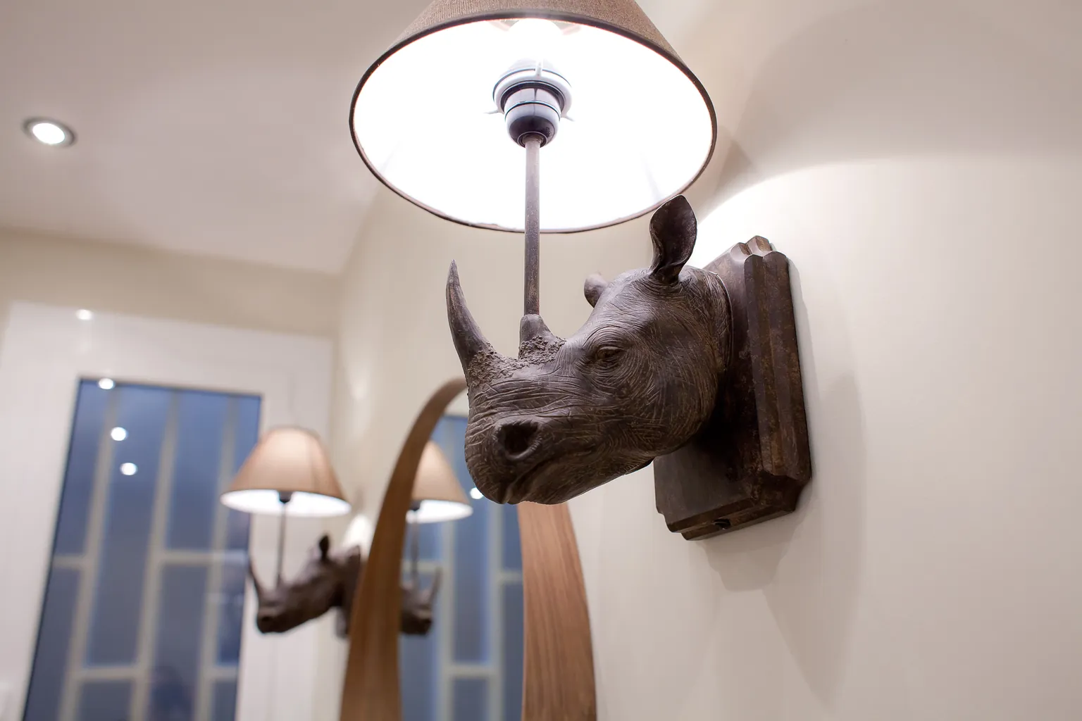 Detalle de un aplique de pared con figura de rinoceronte y pantalla de tela en el recibidor
