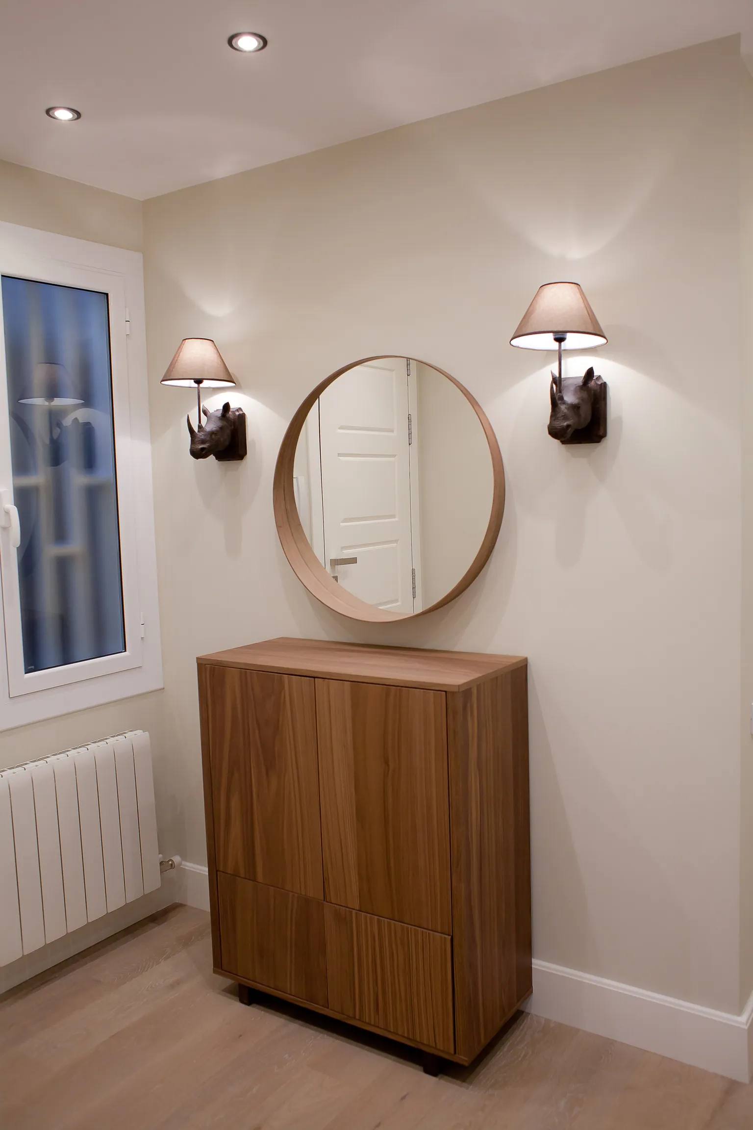 Recibidor con mueble de madera, espejo redondo y dos apliques con figura de rinoceronte