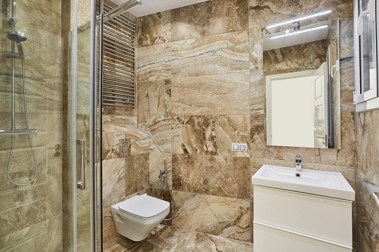 Baño con porcelánico de gran formato efecto mármol marrón, ducha con mampara de vidrio, toallero de acero, inodoro suspendido y mueble blanco