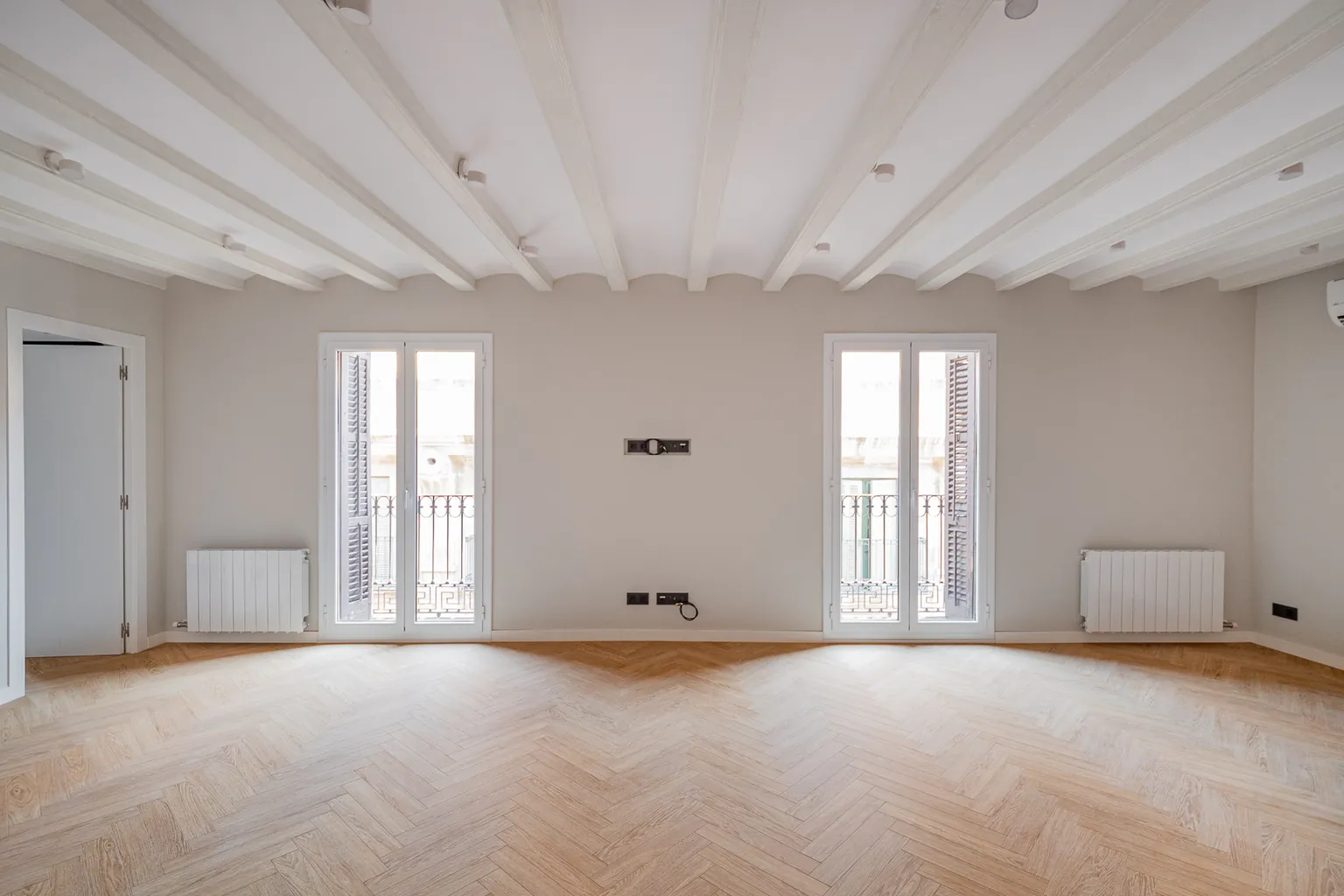 Living room with two balcony doors with louvred shutters, restored beam-and-vault ceiling painted white and herringbone flooring