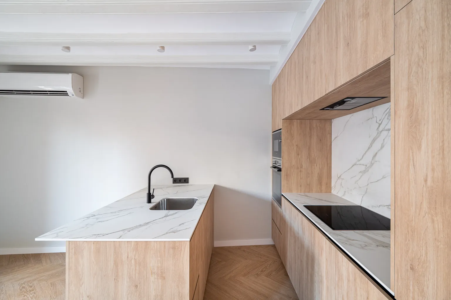 Kitchen island with sink and black tap, marble-effect worktop and induction hob over the herringbone floor