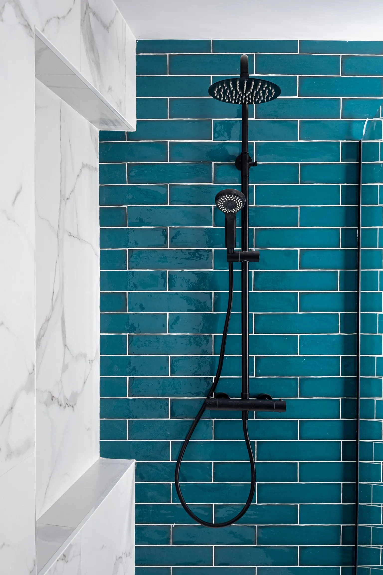 Shower area with blue-green tiles, a black shower column and niches in a white marble-effect finish