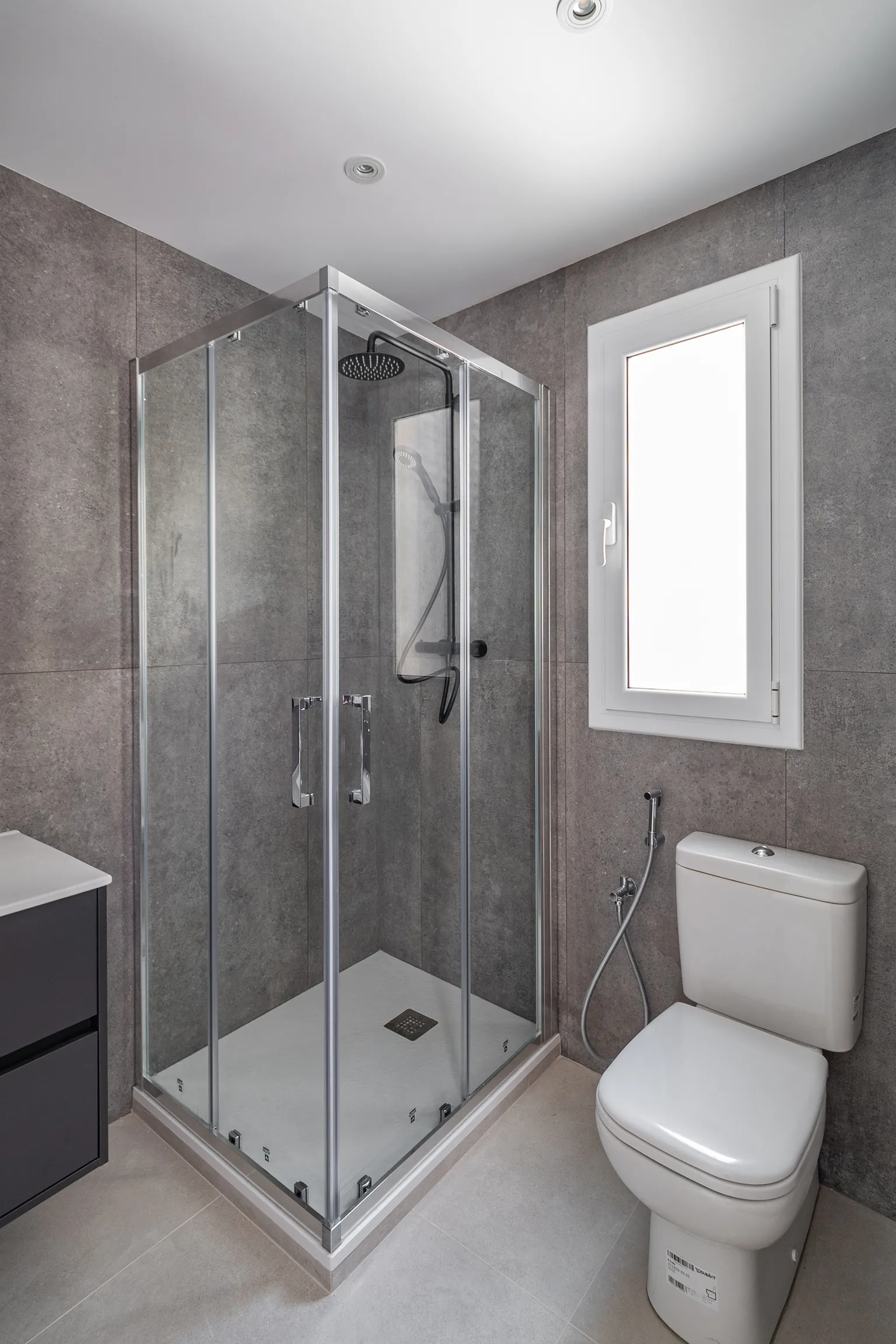 Bathroom with large-format tiles in grey tones, a corner shower with a clear screen, black tapware and a wall-hung vanity
