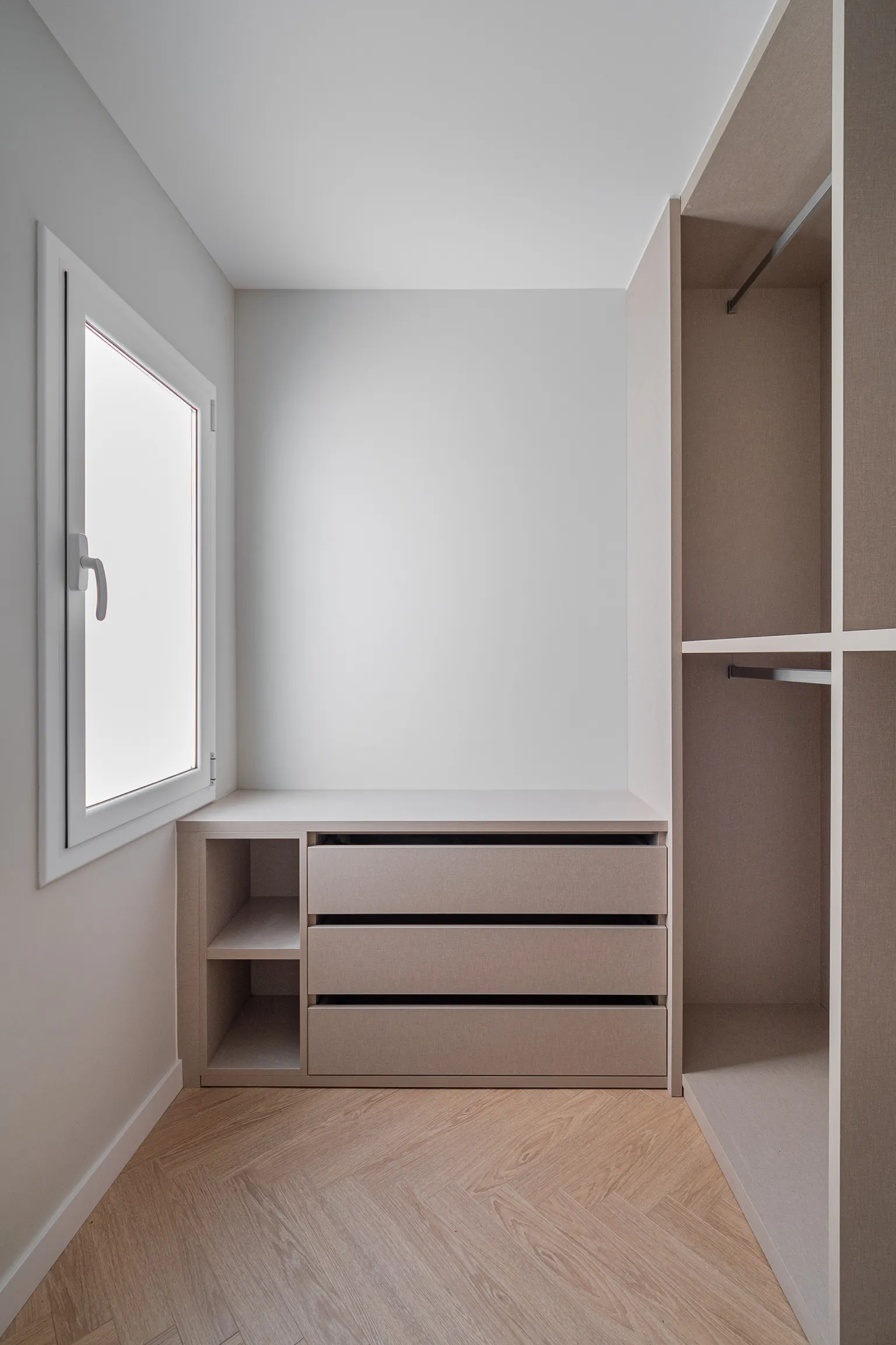 Dressing room with a low unit of drawers and open cubbies under the window, hanging modules and herringbone flooring