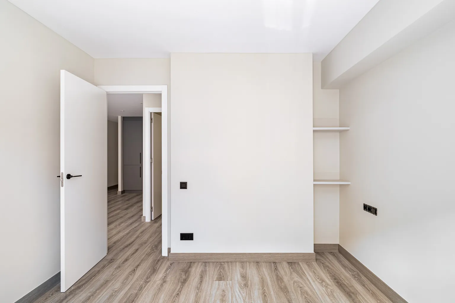 Dormitorio con baldas empotradas en un hueco de la pared y puerta abierta al pasillo