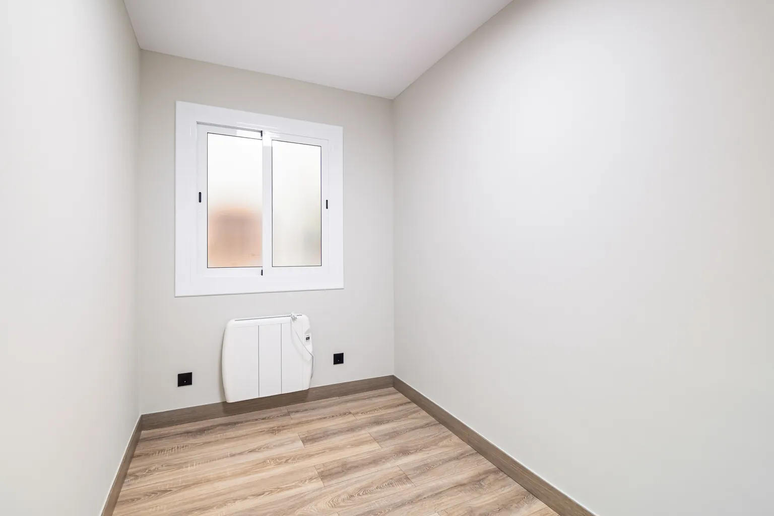 Habitación pequeña con ventana de vidrio translúcido, radiador eléctrico y suelo de aspecto madera